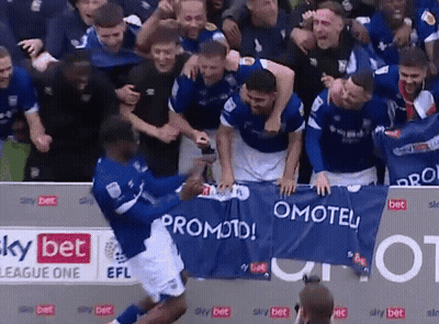 A Group Of Soccer Players Celebrate Behind A Banner That Says Promoted GIF