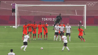 A Group Of Soccer Players On A Field With Tokyo 2020 Written On The Wall Behind Them GIF