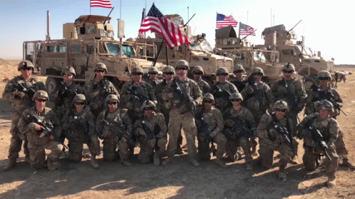 A Group Of Soldiers Are Posing For A Picture In Front Of A Military Vehicle That Says Stryker GIF