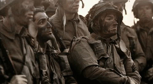 A Group Of Soldiers Are Sitting In A Line And One Of Them Has A Helmet On GIF