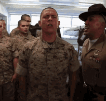 A Group Of Soldiers Are Standing In A Room And One Of Them Is Wearing A Hat That Says Us Marines GIF