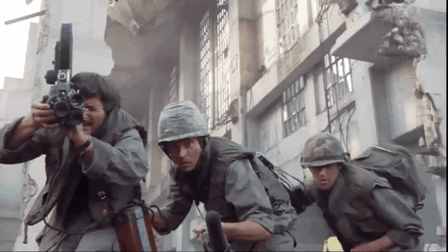 A Group Of Soldiers Are Standing In Front Of A Building And One Is Holding A Camera With The Letter B On It GIF