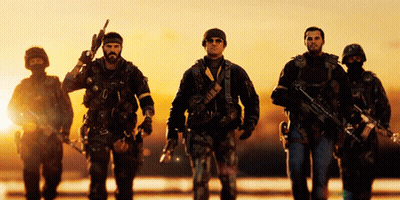 A Group Of Soldiers Are Walking In A Line With One Holding A Gun GIF