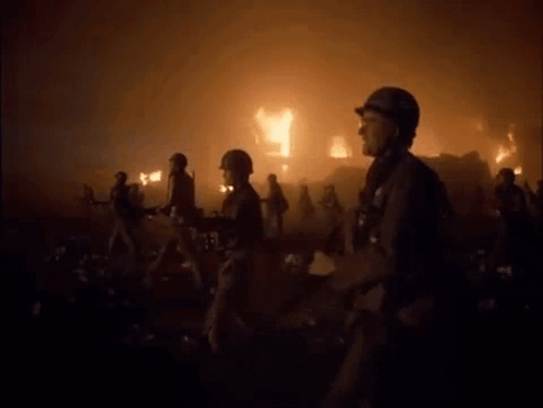 A Group Of Soldiers Are Walking In Front Of A Burning Building GIF