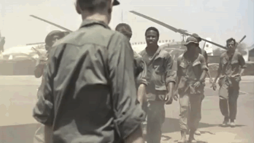 A Group Of Soldiers Are Walking In Front Of A Helicopter GIF
