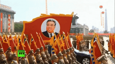 A Group Of Soldiers Marching With Flags And A Picture Of Kim Jong Un GIF