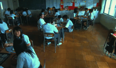 A Group Of Students Are Sitting At Their Desks In A Classroom With A Bulletin Board Behind Them GIF
