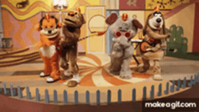 A Group Of Stuffed Animals Are Standing On A Stage With Dominoes In The Background GIF