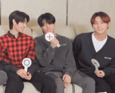 A Group Of Three Young Men Are Sitting On A Couch Holding Signs . GIF