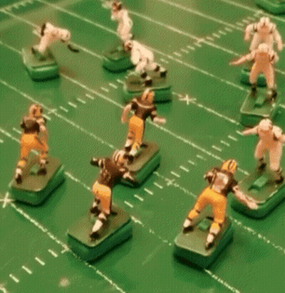 A Group Of Toy Football Players On A Green Field With One Wearing A Black Jersey With The Number 9 On It GIF