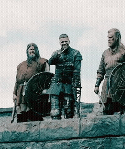 A Group Of Vikings Are Standing On Top Of A Stone Wall Holding Shields . GIF