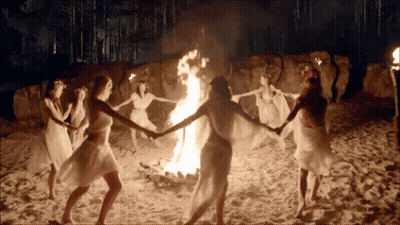 A Group Of Women Are Dancing Around A Fire On The Beach GIF