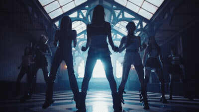 A Group Of Women Are Dancing In A Dark Room With A Light Shining Through The Windows GIF