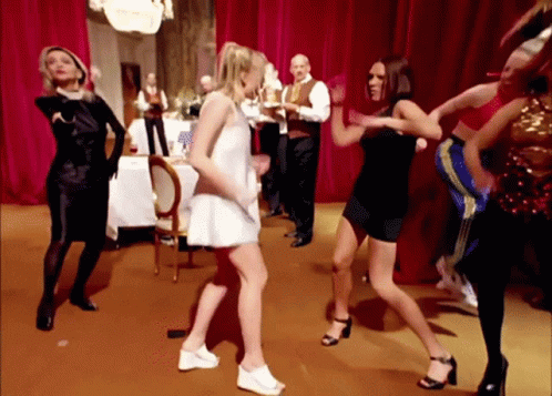A Group Of Women Are Dancing In A Room With Red Curtains . GIF