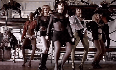 A Group Of Women Are Dancing In A Room With Scaffolding Behind Them . GIF