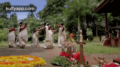 A Group Of Women Are Dancing In Front Of A Floral Display . GIF