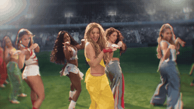 A Group Of Women Are Dancing On A Field With One Wearing A Yellow Outfit GIF
