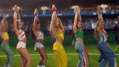 A Group Of Women Are Dancing On A Field With Their Hands In The Air GIF