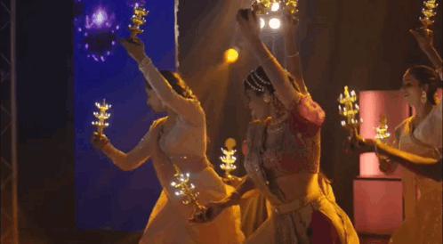 A Group Of Women Are Dancing On A Stage Holding Candles . GIF