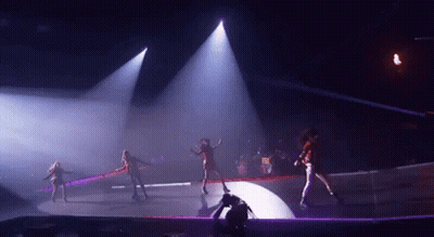A Group Of Women Are Dancing On A Stage In A Dark Room With Purple Lights . GIF