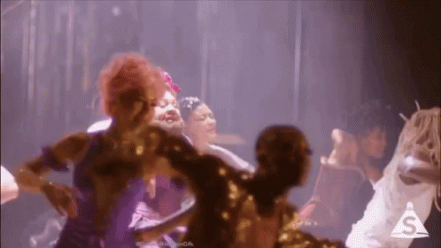 A Group Of Women Are Dancing Together On A Stage In A Dark Room . GIF