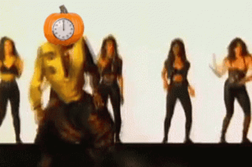 A Group Of Women Are Dancing With A Pumpkin On Their Head That Has A Clock On It GIF