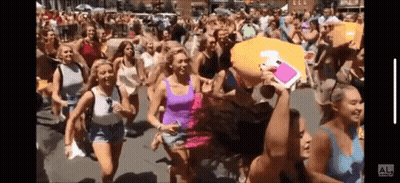 A Group Of Women Are Running Down A Street With A Man Holding A Pillow That Says Al On It GIF