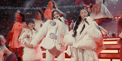 A Group Of Women Are Singing Into Microphones On A Stage With A Red Background GIF