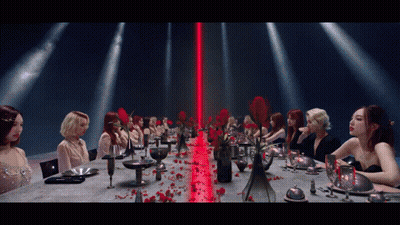 A Group Of Women Are Sitting At A Long Table With A Red Light Behind Them GIF