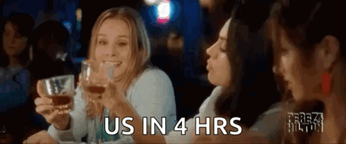 A Group Of Women Are Sitting At A Table Holding Glasses Of Whiskey And Toasting . GIF