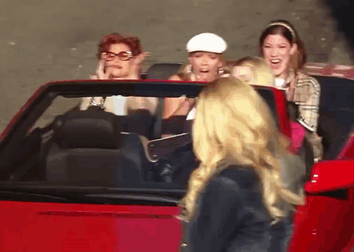 A Group Of Women Are Sitting In A Red Car And One Of Them Is Wearing A White Hat GIF