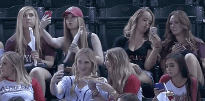 A Group Of Women Are Sitting In A Stadium And One Of Them Is Wearing A Shirt That Says Alpha Chi GIF