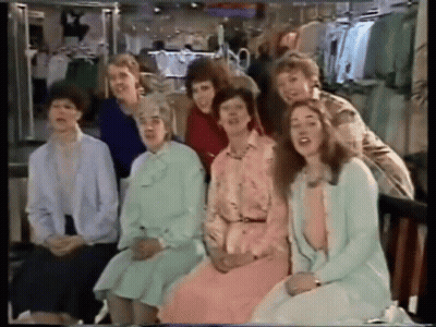 A Group Of Women Are Sitting In Front Of A Clothing Rack GIF