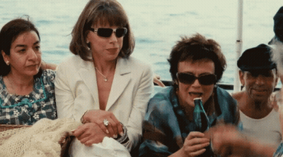 A Group Of Women Are Sitting On A Boat One Of Them Is Drinking From A Bottle GIF