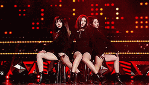A Group Of Women Are Sitting On A Stage In Front Of A Red Background GIF