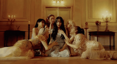 A Group Of Women Are Sitting On The Floor Looking At A Woman In A Blue Dress GIF