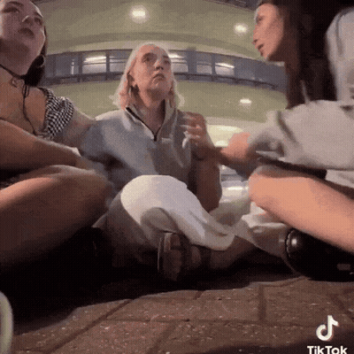 A Group Of Women Are Sitting On The Ground And One Of Them Has A Tiktok Sticker On Her Phone GIF