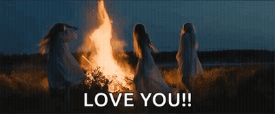A Group Of Women Are Standing Around A Fire In A Field . GIF