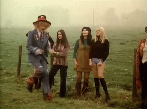 A Group Of Women Are Standing In A Field With A Man In A Blue Suit . GIF