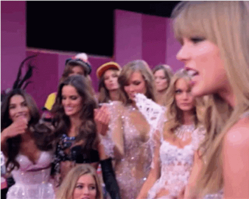 A Group Of Women Are Standing In A Room With A Pink Wall . GIF