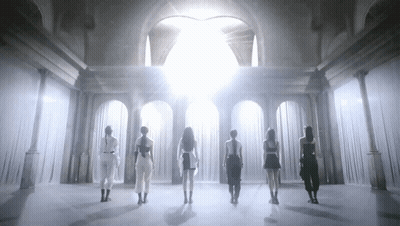 A Group Of Women Are Standing In A Room With White Curtains And A Light Shining Through The Curtains . GIF