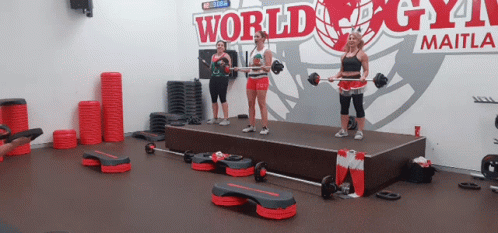 A Group Of Women Are Standing On A Stage In Front Of A Sign That Says World Gym GIF