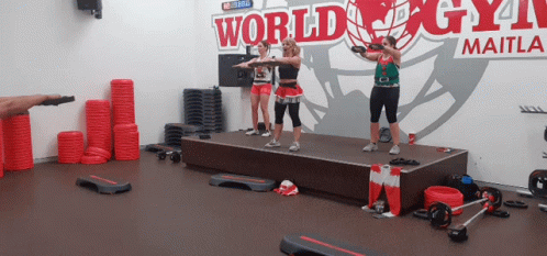 A Group Of Women Are Standing On A Stage In Front Of A World Gym Sign GIF