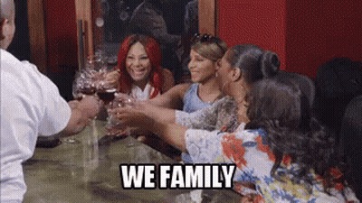 A Group Of Women Are Toasting With Wine Glasses At A Table With The Words `` We Family '' . GIF