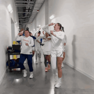 A Group Of Women Are Walking Down A Hallway And One Of Them Is Wearing A White Nike Shirt GIF