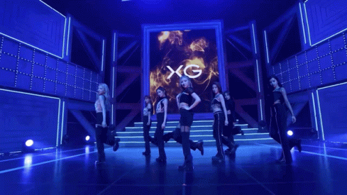 A Group Of Women Dancing In Front Of A Screen That Says Xg On It GIF