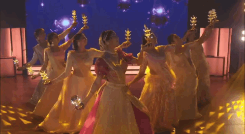 A Group Of Women In Long Dresses Are Dancing On A Stage Holding Candles . GIF