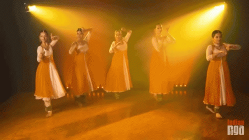 A Group Of Women In Orange And White Dresses Are Dancing In Front Of A Yellow Light And The Words Indian Naga Are On The GIF