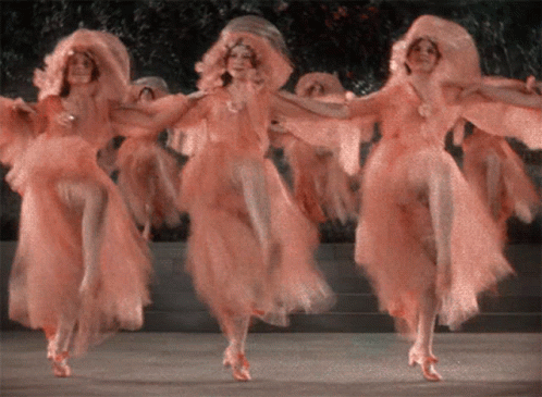 A Group Of Women In Pink Dresses Are Dancing GIF