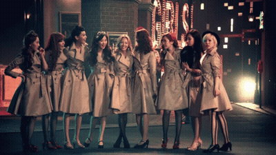 A Group Of Women In Trench Coats Are Standing In A Row GIF